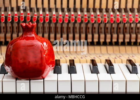 red pomegranate on the close up image of grand piano keys and interior showing strings, hammer and structure background Stock Photo