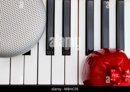 grey stylish speaker and red pomegranate on the black and white piano keys on top view Stock Photo