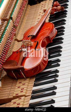 classic brown violin on the close up image of grand piano keys and interior showing strings, hammer and structure background Stock Photo