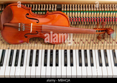 classic brown violin on the close up image of grand piano keys and interior showing strings, hammer and structure background Stock Photo