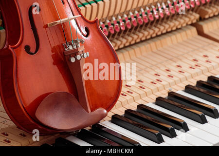 classic brown violin on the close up image of grand piano keys and interior showing strings, hammer and structure background Stock Photo