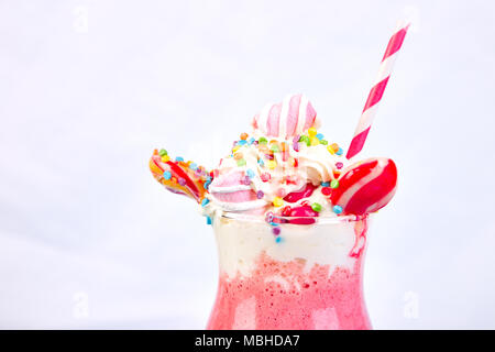 Pink Extreme milkshake with berry, rasberry, strawberry, candy marshmallow, lollipops on blue background.. Crazy freakshake. Copy space. Food trend Ov