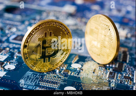 Two bitcoins standing on the electronic motherboard of a laptop Stock Photo