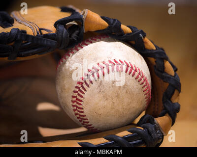 Close up sports background image of an old used weathered leather baseball with red laces inside of a baseball glove or mitt showing intricate details Stock Photo
