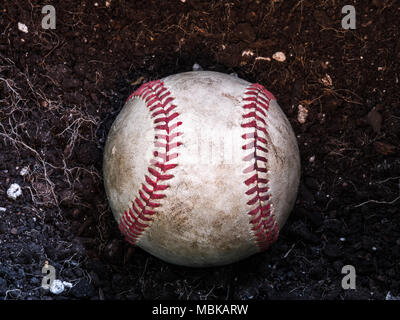 Close up sports background image of an old used weathered leather baseball laying in a pile of brown dirt showing intricate detailing and red laces. Stock Photo
