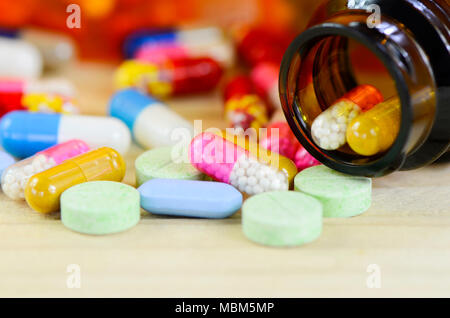 Colorful of oral medications on pine wood table with amber medicine bottle as background. Stock Photo