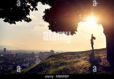 Woman in silhouette with hat rising hand at the sunset city view background. City life concept. Stock Photo