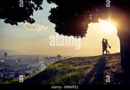 Yong couple in silhouette hugging and looking at the sunset city landscape Stock Photo