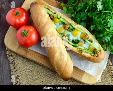 Baked crispy baguette with fried eggs, cucumbers and greens Stock Photo