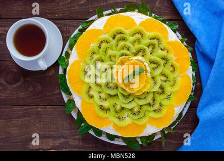 Bright round festive fruit cake decorated with kiwi, orange, mint and a cup of tea. Stock Photo