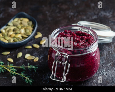 Beetroot pesto or hummus. Homemade beet pesto sauce in glass jar,pumpkin seeds and fresh thyme on dark black background. Copy space for text. Ideas and recipes for healthy vegetarian detox diet food Stock Photo