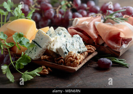 Various cheeses , grapes and prosciutto on a old wooden table. Stock Photo