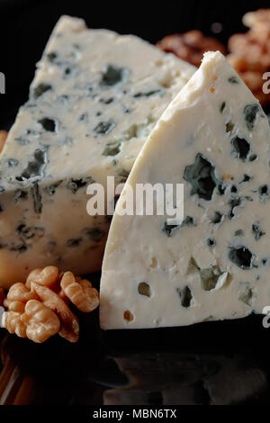 Wedges of soft blue cheese with walnuts on a black plate. Stock Photo