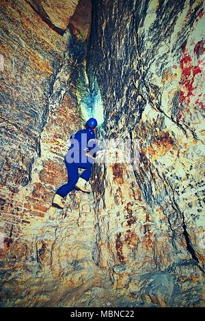 Dry sandstone tunnel, man worker in protective suite in underground. Mysterious dungeon tunnel with walls made inorange sandstone rock Stock Photo