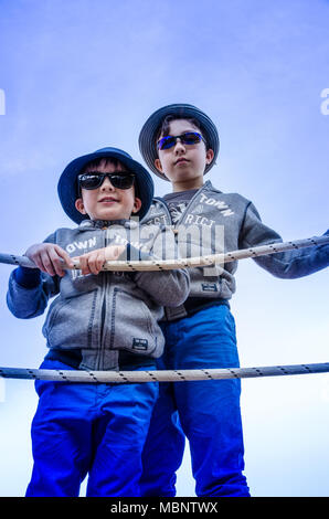 Two young brothers stand next to a rope fence as they pose for a portrait. Stock Photo