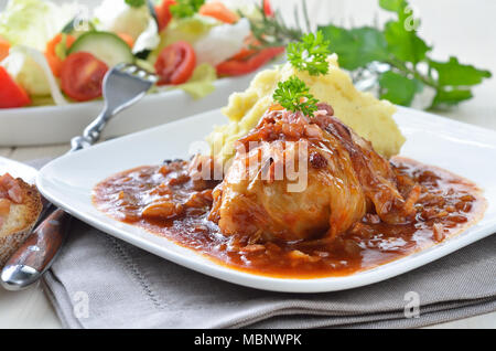 Cabbage leaves stuffed with minced meat, sauce with bacon and onions, purree and salad Stock Photo