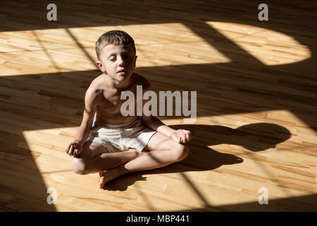 Charming little boy is while doing yoga at home at the day time. Stock Photo