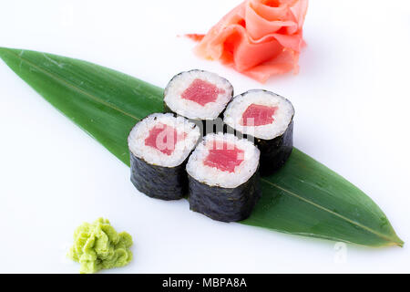Delicious fresh mini-rolls with tuna on a banana leaf. Sushi rolls on a white background with ginger and wasabi. Stock Photo