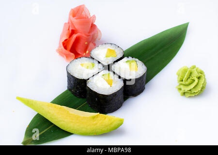 Delicious fresh mini-rolls with avocado and cheese on a banana leaf. Sushi rolls on a white background with ginger and wasabi. The Japanese menu. Stock Photo