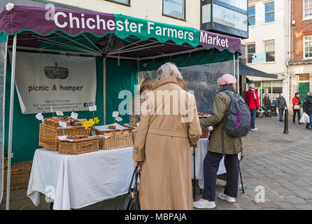 People shopping outside at a market stall at the Chichester Farmers' Market in the shopping centre in Chichester, West Sussex, England, UK. Stock Photo