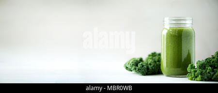 Glass jar mugs with green health smoothie, kale leaves, lime, apple, kiwi, grapes, banana, avocado, lettuce. Copy space, sunlight effect. Raw, vegan, vegetarian, detox, alkaline food concept. Stock Photo