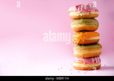 Stack of glazed colorful assorted donuts with sprinkles on pink background. Copy space. Sweet doughnuts for kids Stock Photo
