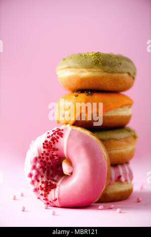 Stack of glazed colorful assorted donuts with sprinkles on pink background. Copy space. Sweet doughnuts for kids Stock Photo