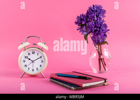 Blog concept image with old clock, notebooks and flowers in a vase on a pink background Stock Photo
