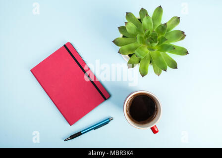 Green plant, red notebook, pen and cup of coffee on blue background. Beauty blog concept photo. Stock Photo