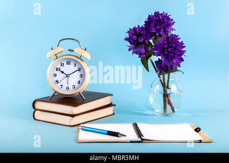 Old clock on books and open notebook isolated by on a blue background Stock Photo