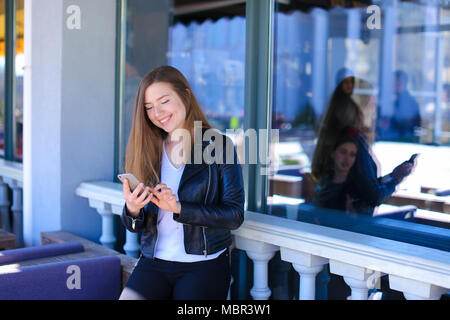 Pretty girl typing message on smartphone at street cafe. Stock Photo
