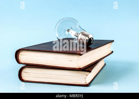 Bulb on two closed books isolated on a blue background Stock Photo