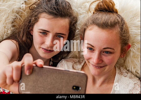 Two happy teenage girls taking a selfie indoors with a smartphone. Stock Photo