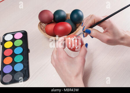Girl hands painting Easter eggs with brush on wooden table. Close up Stock Photo