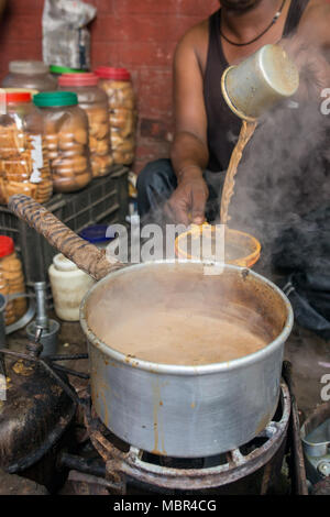 Man pour cup of hot milk tea Indian style or chai for customers in his shop along the street in Kolkata, India Stock Photo