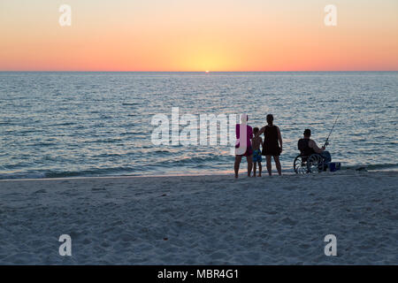 Family on beach at sunset. Man in wheelchair, fishing. Stock Photo