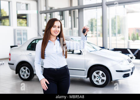 Beautiful business woman standing in modern car dealership and holding car key