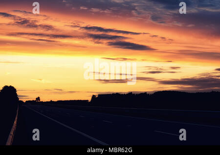 Empty asphalt road and sun rising on skyline. Colorful sunset over road. Minimalist style design. Nature background, landscape with copy space. Banner Stock Photo