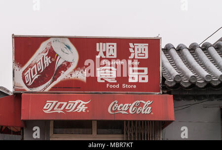 Beijing, China - April 26, 2010: Closeup of red Coca-Cola sign fixed on gray roof against silver sky. Read in English and Mandarin about beer, cigaret Stock Photo