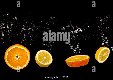 Lemon and orange float in water with bubbles, the fruit is in water splash and isolated on a black background Stock Photo