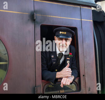 Close up of caucasian senior train guard, in peaked cap, isolated leaning out of vintage railway carriage window giving a happy 'thumbs up'. Stock Photo