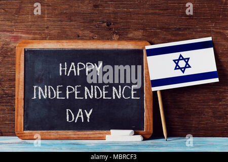 a wooden-framed chalkboard with the text happy independence day written in it, some pieces of chalk and an israeli flag on a rustic wooden surface Stock Photo