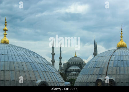 Sultan Ahmed or Blue Mosque seen from Hagia Sophia on a cloudy day highlighting golden dome tips in the Foreground Stock Photo