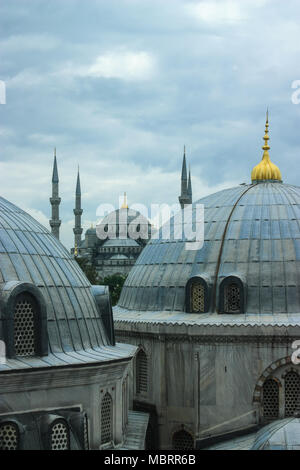 Sultan Ahmed or Blue Mosque seen from Hagia Sophia on a cloudy day highlighting golden dome tips in the Foreground Stock Photo