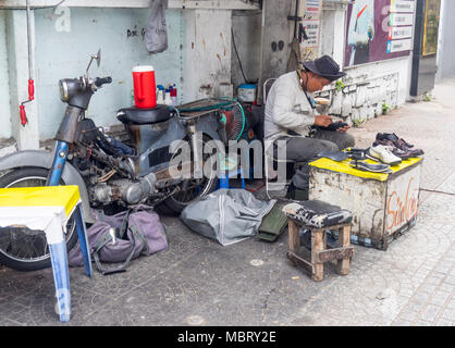 A male Vietnamese cobbler working on the sidewalk, repairing a shoe, Ho Chi Minh City, Vietnam. Stock Photo