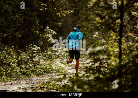 athlete runner in blue sports jacket forest trail in rain Stock Photo