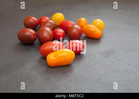 Raw ingredients: cherry and baby plum tomatoes in a variety of colours shown on a slate board Stock Photo