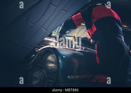 Classic Car Restoration Fix. Caucasian Men Passionate About Vintage Vehicles Trying To Fix Some Issues with His American Classic Car Gasoline Engine. Stock Photo