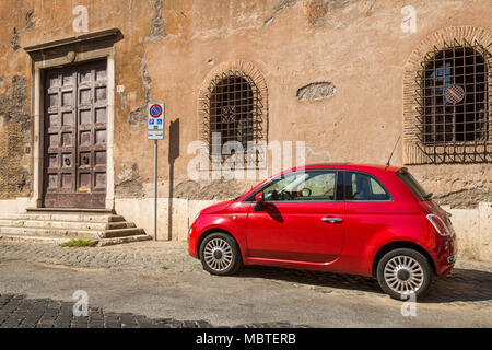 A red Fiat 500 on a partly cobbled street in the Trastevere area of Rome, Italy, it's parked in a disabled parking space as shown by the nearby sign,  Stock Photo