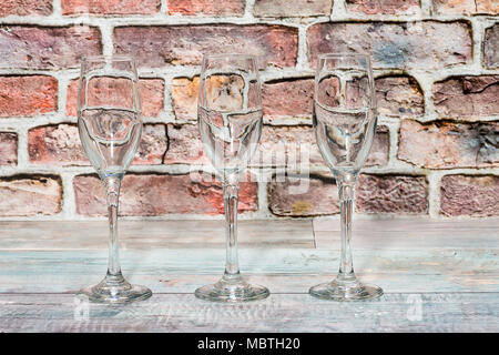 three empty glass goblets on a rustic wooden board and with red bricks background Stock Photo
